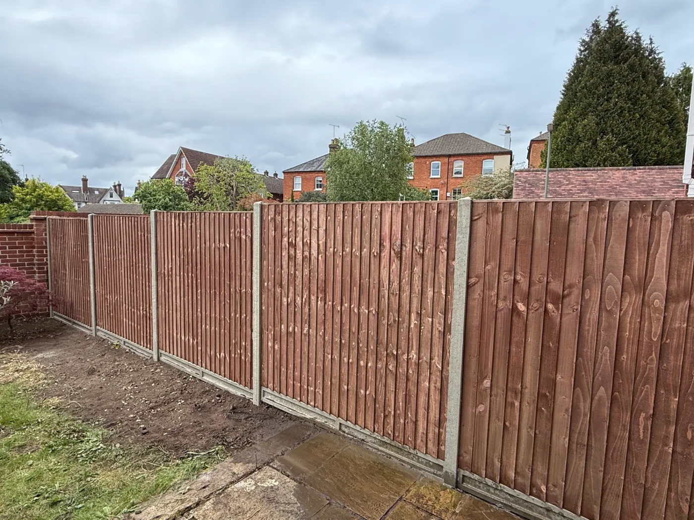 Brown stained closeboard fencing with concrete posts behind a Surrey house
