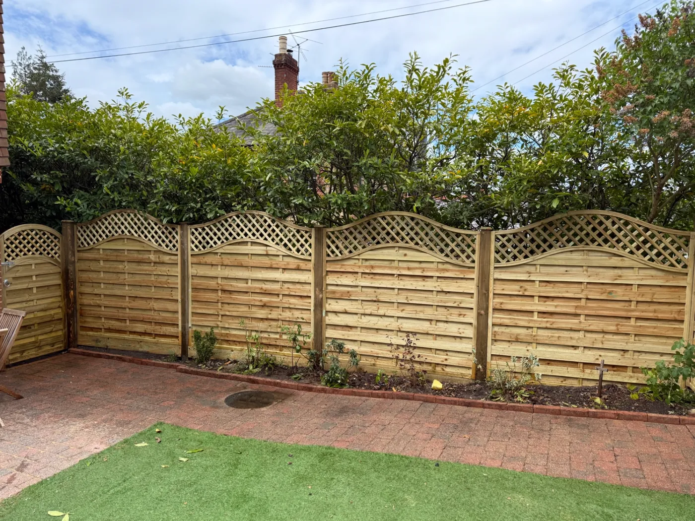 Wavy trellis topped garden fence panels fitted along a patio